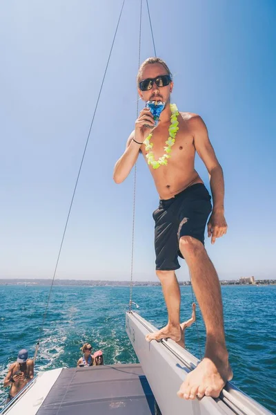 在阳光灿烂的日子里，一只戴着太阳镜站在白船边缘喝果汁的雄鱼 — 图库照片