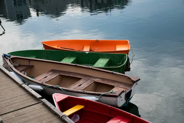Сцена из четырех разноцветных лодок рядом с деревянным берегом озера — стоковое фото