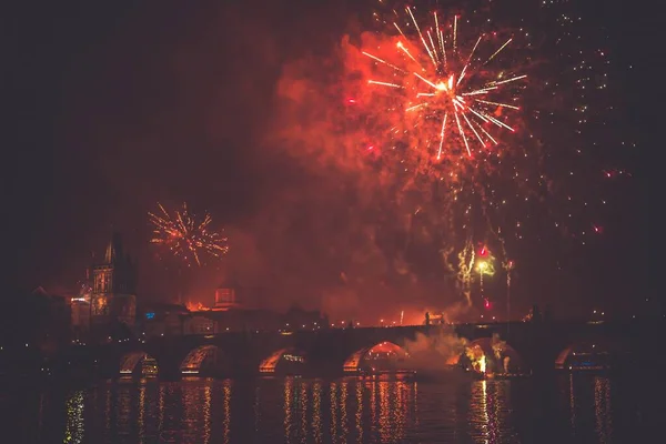 Hermoso disparo de un fuegos artificiales de color rojo en el cielo nocturno sobre un puente en un río —  Fotos de Stock