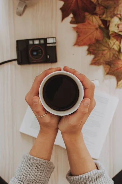 Plan vertical d'une personne tenant une tasse de café avec un appareil photo et laisse en arrière-plan — Photo