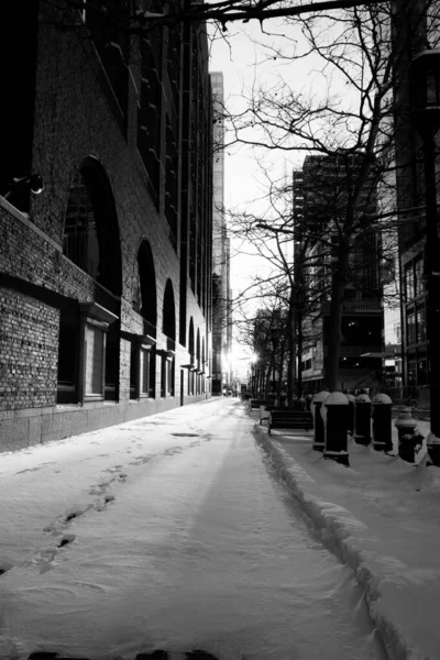 Zwart-wit verticaal schot van een stoep naast een hoog gebouw en menselijke sporen op de sneeuw — Stockfoto