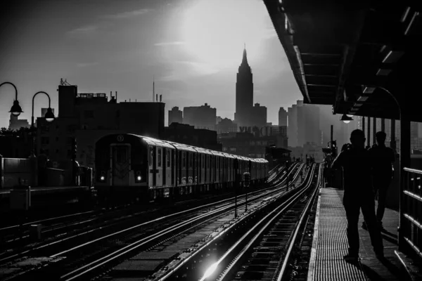 Schwarz-Weiß-Aufnahme eines Bahnhofs mit Menschensilhouetten und einer Stadt im Hintergrund — Stockfoto