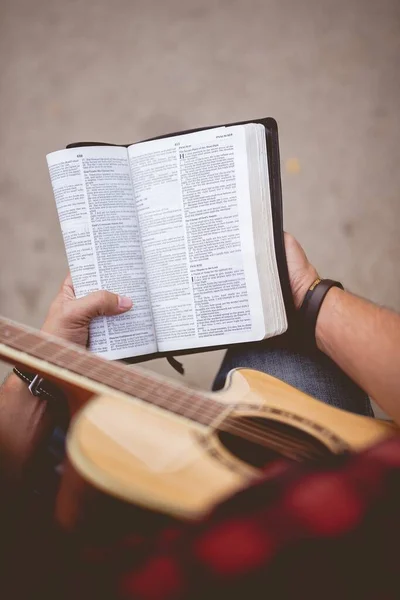 Boven verticaal schot van een persoon zittend met zijn gitaar en het lezen van een bijbel — Stockfoto