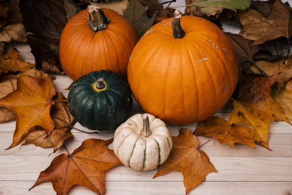 Alto ángulo de tiro de calabazas rodeadas de hojas marrones en una superficie de madera para Halloween — Foto de Stock