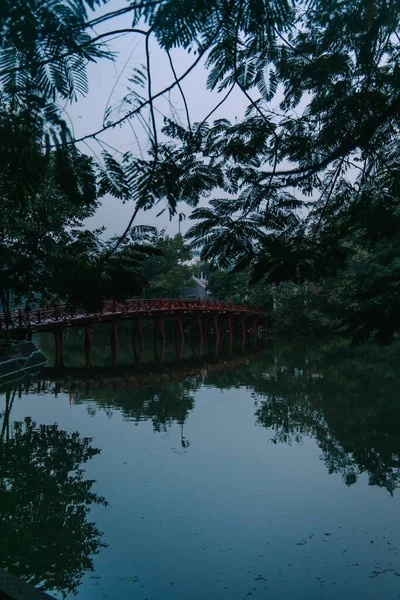 Eine rote Brücke, die sich im See spiegelt, umgeben von grünen Bäumen unter dem klaren Himmel am Abend — Stockfoto