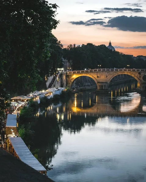 在河中倒映着的桥上，令人叹为观止的夕阳西下，到处都是美丽的灯光 — 图库照片