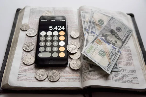 Nagy szög lövés egy nyitott biblia dollár számlák és okostelefon tetején — Stock Fotó