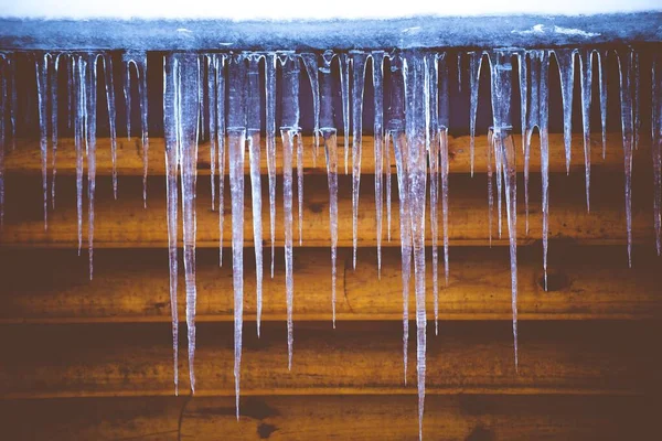Nahaufnahme von Eiszyklen mit einer Holzwand im Hintergrund — Stockfoto