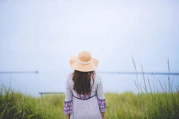 Vrouw met een zomerhoed terwijl ze in de verte kijkt en in een grasveld staat — Stockfoto
