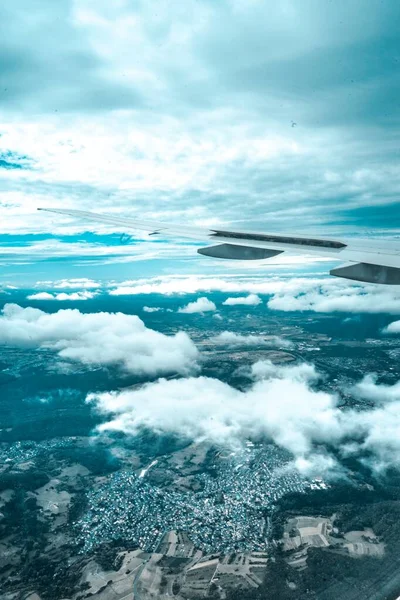 Vertikale Aufnahme eines Flugzeugflügels von innen, umgeben von Wolken und der Stadt darunter — Stockfoto