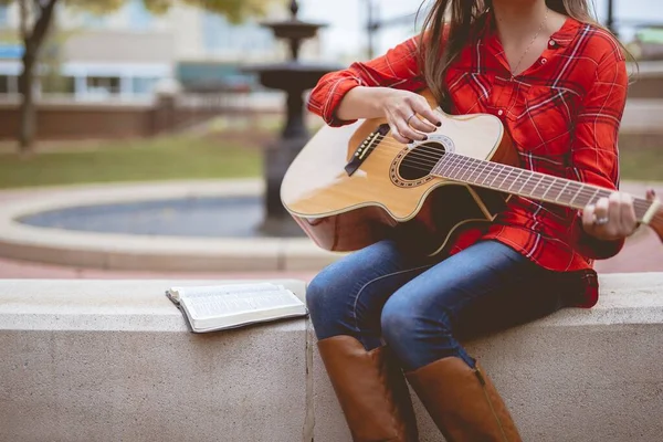 Nő ül egy könyv mellett, miközben játszik a gitár homályos háttérrel — Stock Fotó