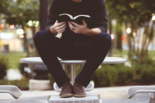 Чоловік сидить на парковому столі і читає Біблію з розмитим тлом — стокове фото