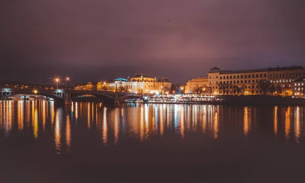 Gyönyörű kép egy városról a folyó mellett és egy hídról balra, a lila égbolttal a tetején. — Stock Fotó