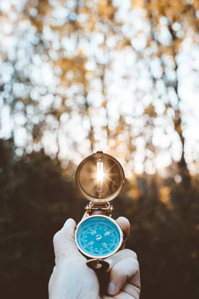 Tiro vertical de uma pessoa segurando uma bússola com o sol brilhando através do buraco — Fotografia de Stock