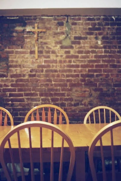 탁자 옆에 있는 나무 의자들 과 벽에 걸려 있는 십자가 조각품의 수직 사진 — 스톡 사진