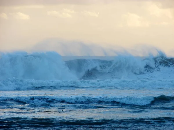 Hermosa toma de las olas del mar salpicando a la orilla durante la puesta del sol —  Fotos de Stock