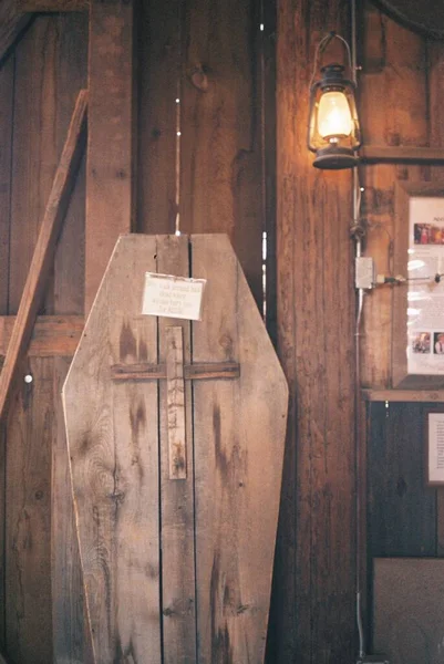 Pionowe ujęcie trumny wykonanej ze sklejki z rzeźbą krzyżową i żarówką wiszącą na drzwiach — Zdjęcie stockowe