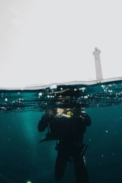 Turkuaz Suda Dalgıcın Dikey Görüntüsü Arka Planda Bir Deniz Feneri — Stok fotoğraf