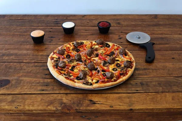 A closeup shot of a pizza with sauces and a cutter on a wooden table