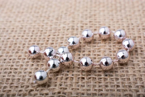 A closeup of a silver ball chain on a burlap surface