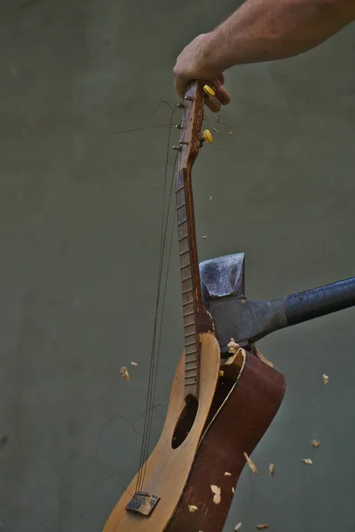 A vertical shot of a person breaking the guitar with an ax