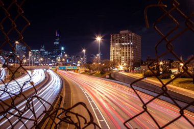 A long exposure shot of the cars on a highway captured through the fences at night in Chicago, USA clipart