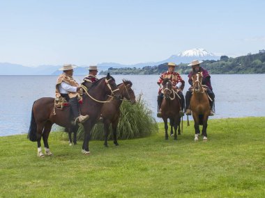 FRUTILLAR, CHILE - Feb 02, 2018: Group of Chilean cowboys called huasos, in their mounts in front of Lake LLanquihue clipart