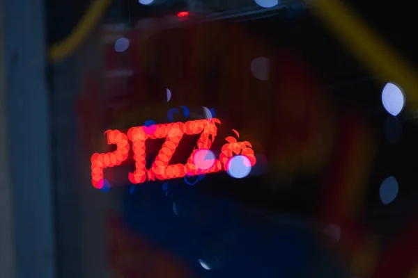 一个发光的红色比萨饼标志的特写镜头穿过玻璃窗 玻璃窗上有彩灯 — 图库照片
