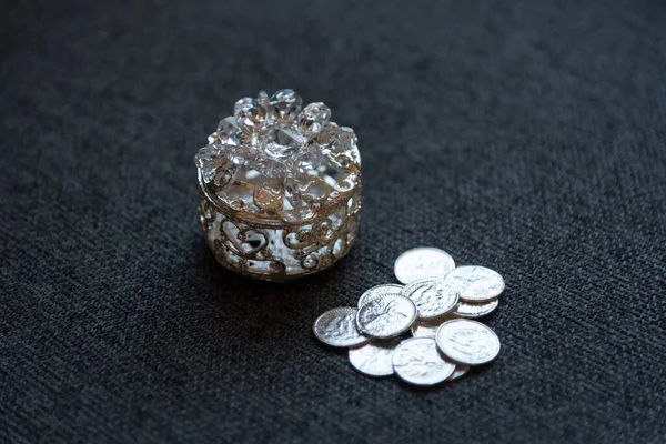 一只漂亮的银色珠宝盒的特写镜头 它在黑色面料上的银币旁边装饰着小天鹅 — 图库照片