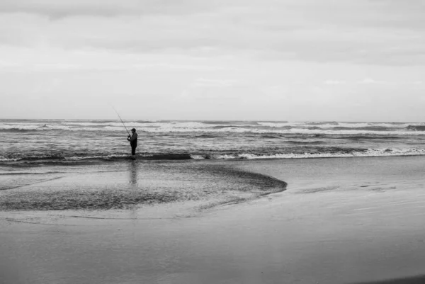 一个孤独的人在黑暗的云彩下在海滩上散步的灰白照片 — 图库照片