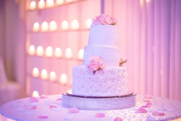 A leaning three tiered cake with buttercream roses at the base and topped with fresh pink flowers