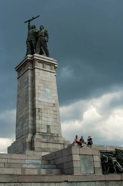 Colpo Verticale Monumento Alto Alcune Persone Sedute Accanto Suo Piedistallo — Foto Stock