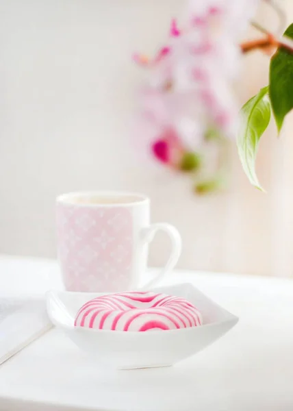 照明の下でマグカップでテーブルの上にボウルにピンクと白の釉薬ドーナツの垂直ショット — ストック写真