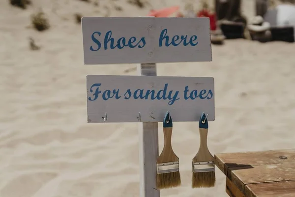 Closeup Shot White Blue Sign Shoes Here Sandy Toes Beach — Stock Photo, Image