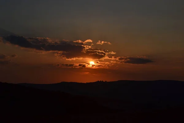 雲の後ろの美しい夕日の下の丘のシルエットの低角度ショット — ストック写真