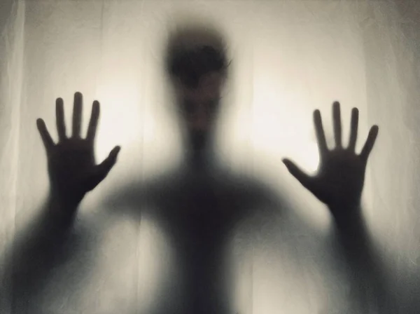 A view of a person standing behind a blurry window with hands on the window - concept: scary