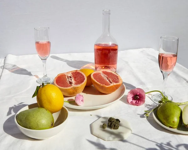 THC CBD Marijuana Flower with Grapefruit, lemons, pears and Pink Rose\' on Table. White linen tablecloth with White/Gray Background.