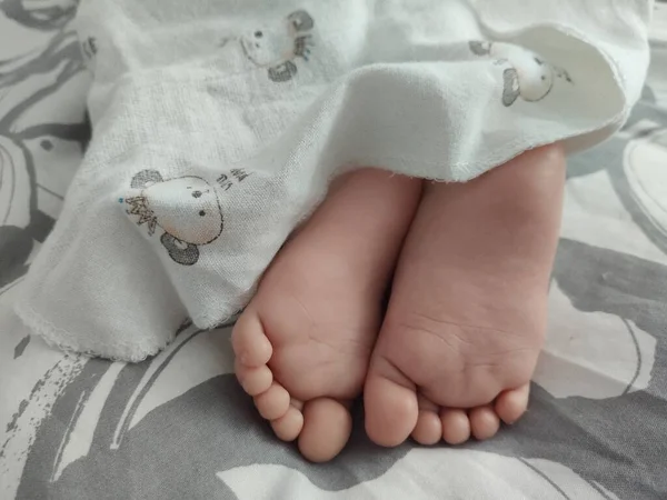 昼間にベッドのカバーの下に赤ちゃんの足のクローズアップショット — ストック写真