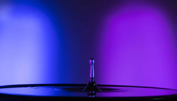 A horizontal shot of a single water drop with purple and blue lighting
