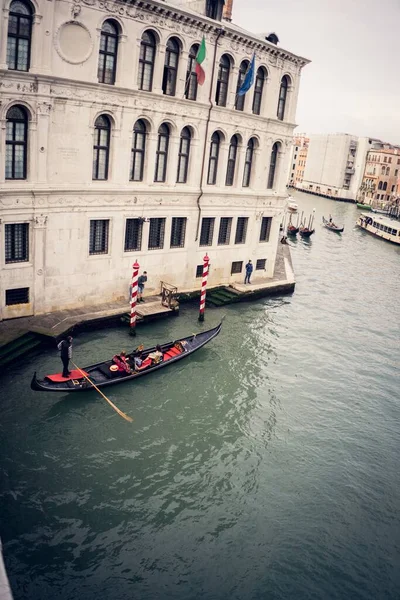 イタリアのヴェネツィアの建物の隣にある壮大なチャンネルで航海する赤いゴンドラの垂直写真 — ストック写真