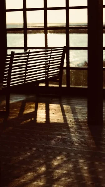 A vertical shot of a wooden bench in a beach house with old windows and the beautiful view of the sea in the background