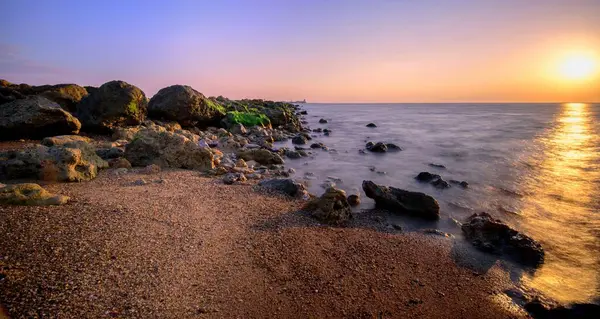 息をのむような夕日の下で輝く砂と岩のビーチのショット — ストック写真