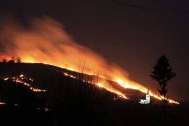 fire on the hill near a village at night clipart