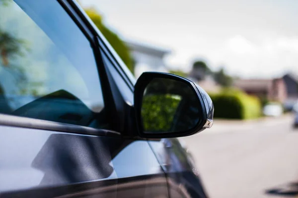 A side-mirror of a black car and the residential street in the blurred background