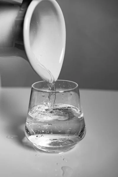 白い表面にセラミックピッチャーから水で満たされているガラスの垂直ショット — ストック写真