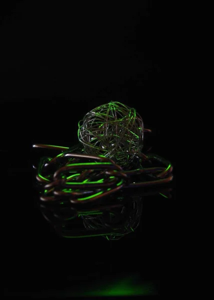 暗い背景のチェーンと金属アートボールの垂直ショットとそれらに輝く緑の光 — ストック写真