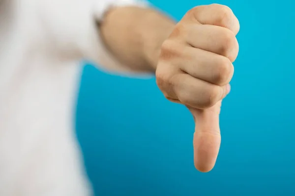 A closeup of a person doing the thumbs-down gesture under the lights against a blue background
