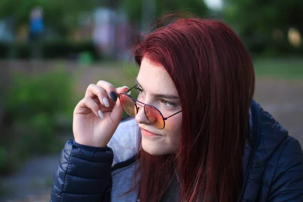 一个红头发女人的画像 她把太阳镜举到眼睛上 同时注意到左边有什么东西 — 图库照片