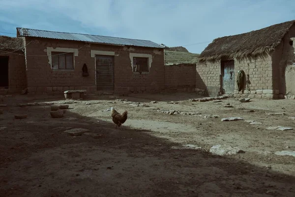 A horizontal shot of a village with mud houses and a chicken running free on a gloomy day