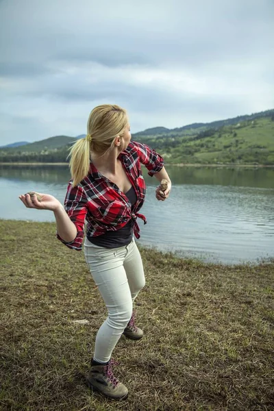 A young blonde woman throwing stones into the water